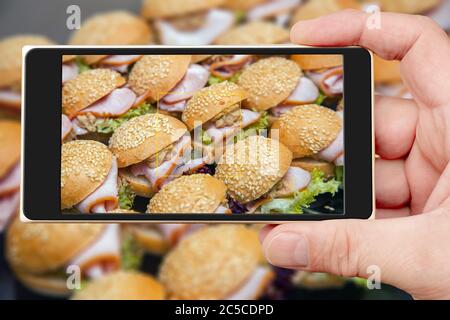 Sandwiches auf dem Smartphone-Bildschirm. Kalte Vorspeisen auf Tablett. Hamburger mit Speck und Kräutern in mehreren Reihen. Stockfoto