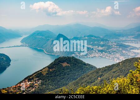Das Dorf Bre, Lugano See und berühmte Berge dieser Gegend. Schöne Luftaufnahme von einem großen See, Schweizer Dorf und umliegenden Bergen. Stockfoto