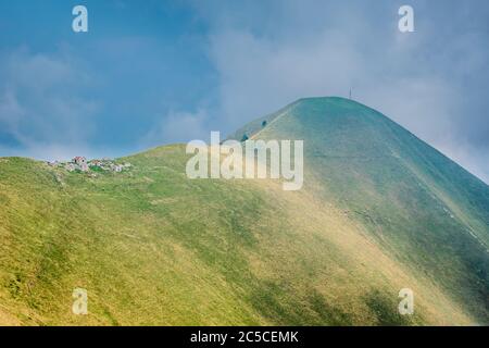 Grüner Hügel mit steilen Hängen, eine alte verlassene Steinfarm auf dem Grat. Wanderweg führt zu einem Gipfel mit einem Kreuz, Monte Crocione, Italien. Stockfoto