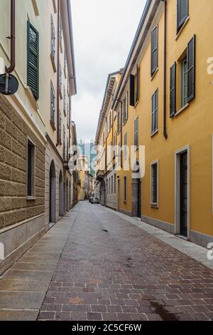 Blick auf eine schmale, leere Straße mit pastellfarbenen bunten Häuserfassaden in Como, Italien.