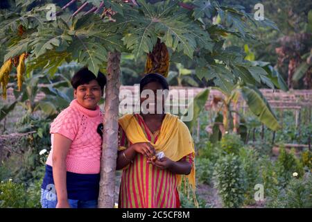 Zwei schöne Teenager lächelnde indische Mädchen stehen unter einer Papiya-Pflanze, selektive Fokussierung Stockfoto