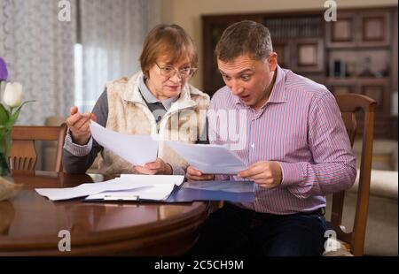 Ältere Frau mit ihrem erwachsenen Sohn, der zu Hause Dokumente ausfüllt Stockfoto