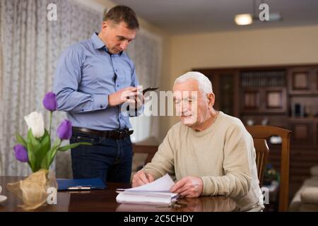 Beunruhigte ältere Mann diskutiert Dokumente mit seinem erwachsenen Sohn, während sie am Tisch zu Hause sitzen Stockfoto