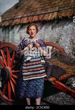 Ein Autochromportrait aus den frühen 1920er Jahren eine Frau aus der Grafschaft Donegal, die einen Wollpullover vor einem traditionellen Häuschen im Dorf Ardara hält. Ursprünglich fotografiert von Clifton Adams (1890-1934) für 'Ireland: The Rock Whence I Was Hewn', eine National Geographic Magazine-Spielfilm vom März 1927. Stockfoto