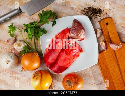 Zutaten zum Kochen. Rohe Hammellunge und Herz mit Zwiebel, Knoblauch, Gewürzen und Kräutern auf Holztisch Stockfoto