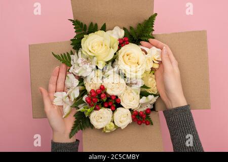 Teilansicht der Frau berühren Blumenstrauß in Karton auf rosa Hintergrund Stockfoto