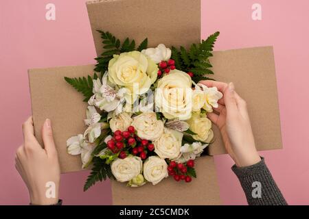 Teilansicht der Frau berühren Blumenstrauß in Karton auf rosa Hintergrund Stockfoto