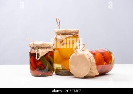 Hausgemachte leckere eingelegte Tomaten und Chili-Paprika in Gläsern auf grau isoliert Stockfoto