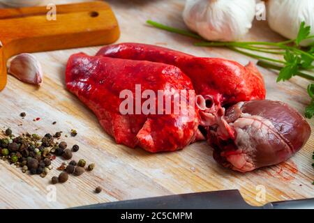 Rohes Lammherz und Lunge bereit zum Kochen mit frischem Gemüse, Gemüse und Gewürzen auf Holzoberfläche Stockfoto