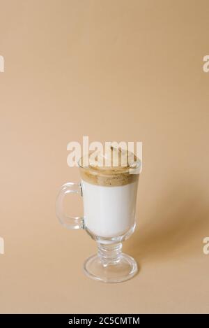 Schöner Dalgon Drink Kaffee mit Schaum in einem transparenten Becher auf beigem Hintergrund Stockfoto