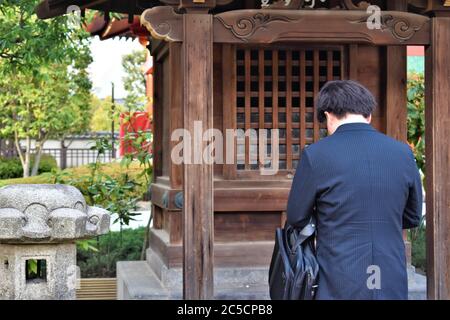 Ein asiatischer Mann in einem blauen Anzug verbeugt sich im Gebet in einem Schrein Stockfoto