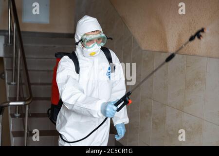 UKRAINE, KIEW - 20. Mai 2020: Der Mensch in einem weißen Schutzanzug und einer weißen Maske desinfiziert Innenflächen in Gebäuden während der Coronavirus-Epidemie Stockfoto