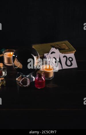 Kristallkugel mit mystischen und okkulten Objekten auf Holz und schwarzem Hintergrund Stockfoto