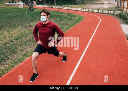 Sportler in medizinischer Maske tun Ausfallschritte beim Arbeiten auf Laufweg im Park Stockfoto