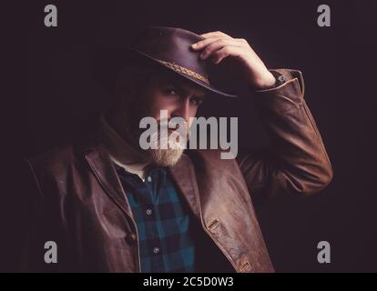 Cowboy in grünem Hemd, Lederjacke und Hut zeigt sein kleines Lächeln und berührt seinen Hut Stockfoto