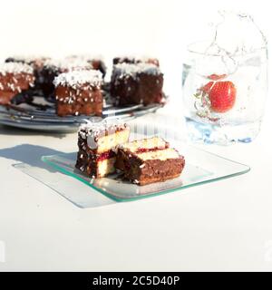 Traditionelle australische lamington Kuchen mit Erdbeermarmelade, Schokolade und Kokosnuss. Gegen ein Glas Wasser, ein Spritzer Wasser, fallen Stockfoto