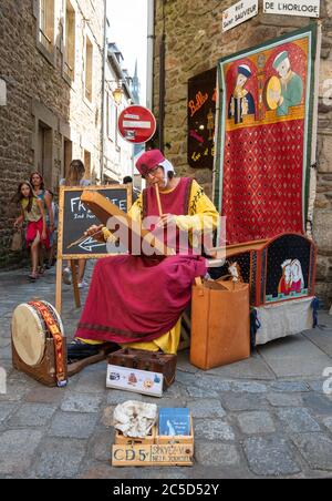 DINAN, FRANKREICH - 4. AUGUST 2018: Straßenkünstler spielt mittelalterliche Musik in der Altstadt von Dinan in der Bretagne. Stockfoto