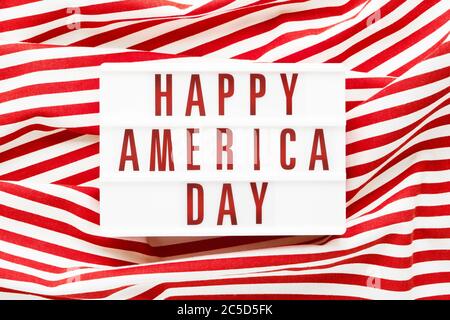 HAPPY AMERICA DAY in Leuchtkasten auf rotem Hintergrund geschrieben. Draufsicht, Kopierbereich. Konzept des Unabhängigkeitstages Stockfoto