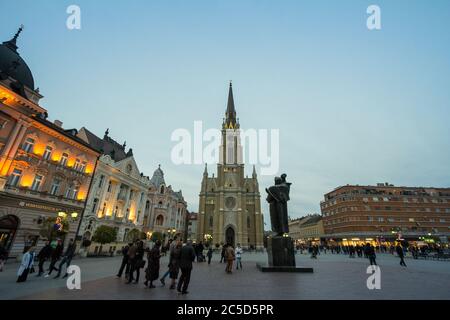 Novi SAD, SERBIEN - 26. NOVEMBER 2016: Der Name der Marienkirche, Novi Sad catholic Cathedral in der Abenddämmerung mit einer Menschenmenge, die auf dem Trg Slobode Platz spazieren geht. Das ist etwa so Stockfoto