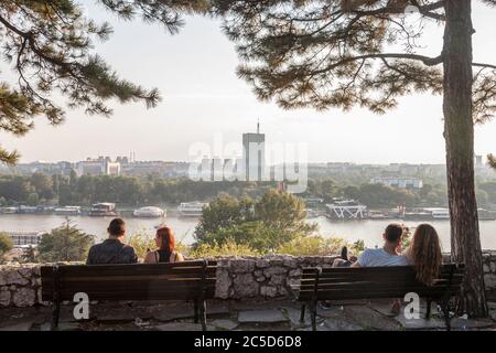 BELGRAD, SERBIEN - 11. JULI 2018: Zwei Liebespaare sitzen auf Bänken und beobachten Neubelgrade (Novi Beograd) bei Sonnenuntergang, mit dem Usce-Turm im Fro Stockfoto