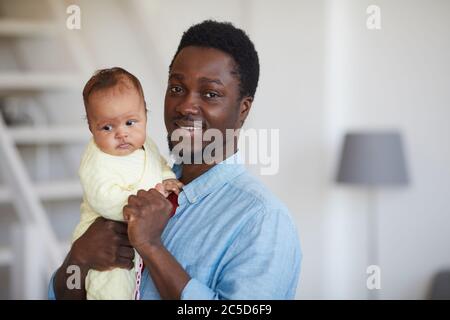 Porträt eines glücklichen afrikanischen Vaters, der das Baby an den Händen hält und die Kamera anlächelt Stockfoto