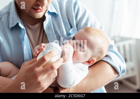 Beschnittene Ansicht des jungen Vaters Fütterung niedlichen Baby junge mit Milch aus Babyflasche Stockfoto