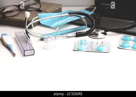 Arbeitsplatz eines Arztes. Laptop, Stethoskop, Pillen, Thermometer, Schutzmaske in blauen Farbtönen auf einem weißen Tisch. Stockfoto