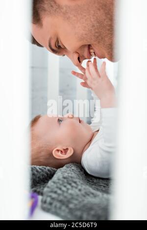 Selektive Fokus von niedlichen Baby im Kinderbett liegen und berühren Gesicht von lächelnden Vater Stockfoto