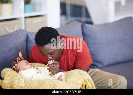 Afrikanischer Vater küsst die Hand des Neugeborenen, während er schläft sie sind im Wohnzimmer zu Hause Stockfoto