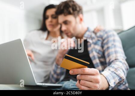 Selektiver Fokus des Mannes, der Kreditkarte hält, während er Laptop in der Nähe der Freundin zu Hause benutzt Stockfoto