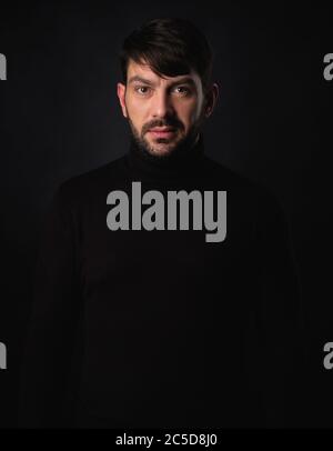 Porträt eines hübschen bärtigen Mannes mit Rollkragen über schwarzem Studiohintergrund Stockfoto