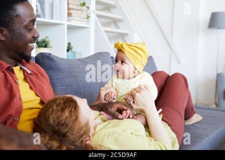 Glückliche Eltern spielen mit ihrem Baby Mädchen, während sie sich auf dem Sofa im Wohnzimmer ausruhen Stockfoto