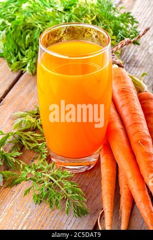 Gesunder Saft aus Bio-Karotten aus dem Garten, mit frischer Karotten-Dekoration mit Blättern, auf rustikalem Holzboden. Stockfoto