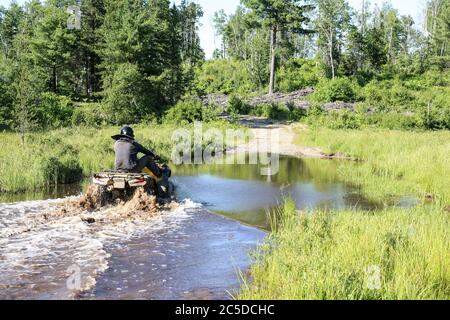 Mann fährt Motocross ATV Quad durch spritzenden Fluss See Wasser. Foy, Sudbury, Ontario, Kanada. Stockfoto