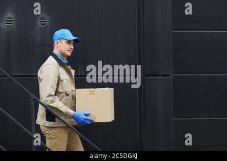 Junger Kurier in Uniform, der die Treppe hinunter geht und den Kasten trägt Stockfoto