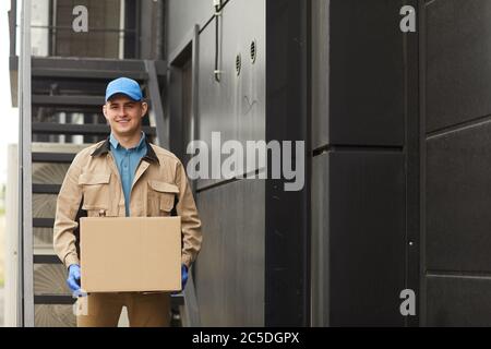 Porträt von jungen Zusteller in Uniform halten Paket und lächeln an der Kamera im Freien Stockfoto