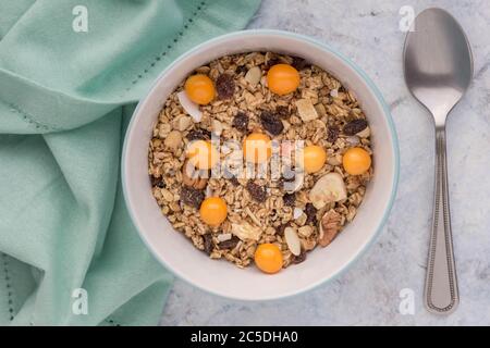 Granola in Schüssel mit Rosinen, getrockneten Bananen, Nüssen und Cape Stachelbeeren - Draufsicht Frühstück Müsli Hintergrund Stockfoto