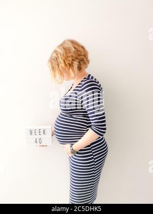 Schwangere junge kaukasische Frau berührt ihren wachsenden Bauch und hält ein Zeichen mit 40 Wochen Stockfoto