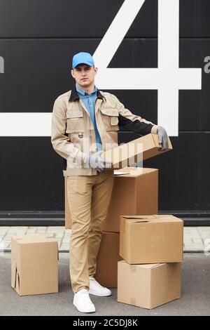 Porträt eines jungen Kuriers in Uniform Blick auf Kamera während der Arbeit mit Paketen im Lager Stockfoto