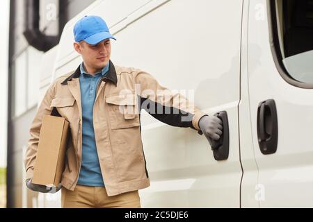 Junger Kurier in Uniform, der Pakete mit dem Van liefert Stockfoto