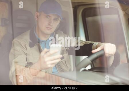 Porträt eines jungen Kuriers, der hinter dem Steuer im Van sitzt und sein Handy benutzt Stockfoto
