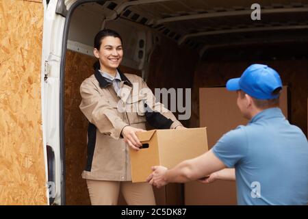 Lächelnde junge Frau, die ihrem Kollegen einen Karton gab, sie entladen Kartons aus dem Van im Freien Stockfoto