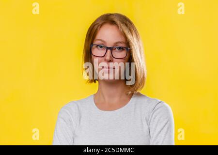 Ein Porträt einer jungen blonden Frau in einer Brille, die mit gekreuzten Armen posiert. Gelber Hintergrund. Speicherplatz kopieren. Stockfoto