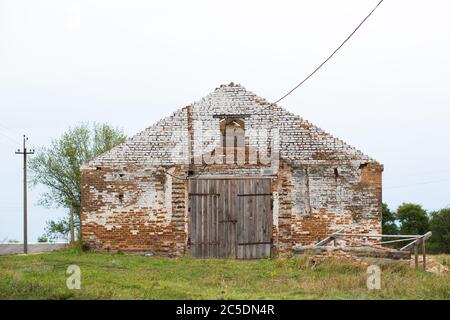 Alte Kuhstall. Großes Holztor und getrocknetes Holz. Altes Ziegelgebäude. Stockfoto