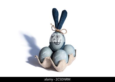 Ostereier in Betonfarbe in Pappschale und osterhase mit blauen Denim-Ohren auf weißem Hintergrund. Frohe Ostern Konzept. DIY-Idee Stockfoto