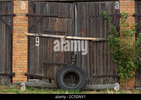 Alte Kuhstall. Großes Holztor und getrocknetes Holz. Altes Ziegelgebäude. Stockfoto