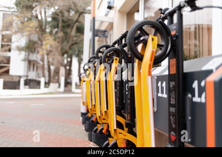 Die Öko-Fahrzeuge. Orange Elektroroller in einer Reihe am Stadttransport-Mietschalter. Draußen, Straße. Horizontale Ausrichtung. Stockfoto