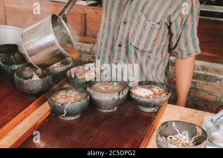 Koch verwendet Lurik Uniform Gießen einer Suppe in soto bathok in Yogyakarta Stockfoto