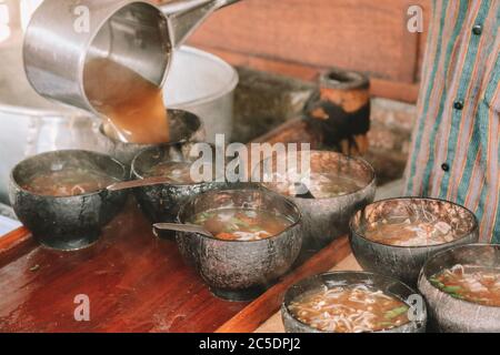 Koch verwendet Lurik Uniform Gießen einer Suppe in soto bathok in Yogyakarta Stockfoto