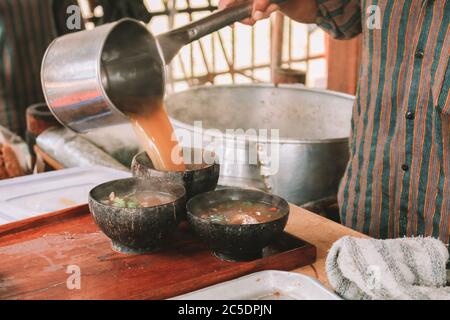 Koch verwendet Lurik Uniform Gießen einer Suppe in soto bathok in Yogyakarta Stockfoto